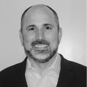 Black and white portrait of Bryan Wolfe, Board Member at Post Acute Analytics, in a dark blazer and open-collar white shirt