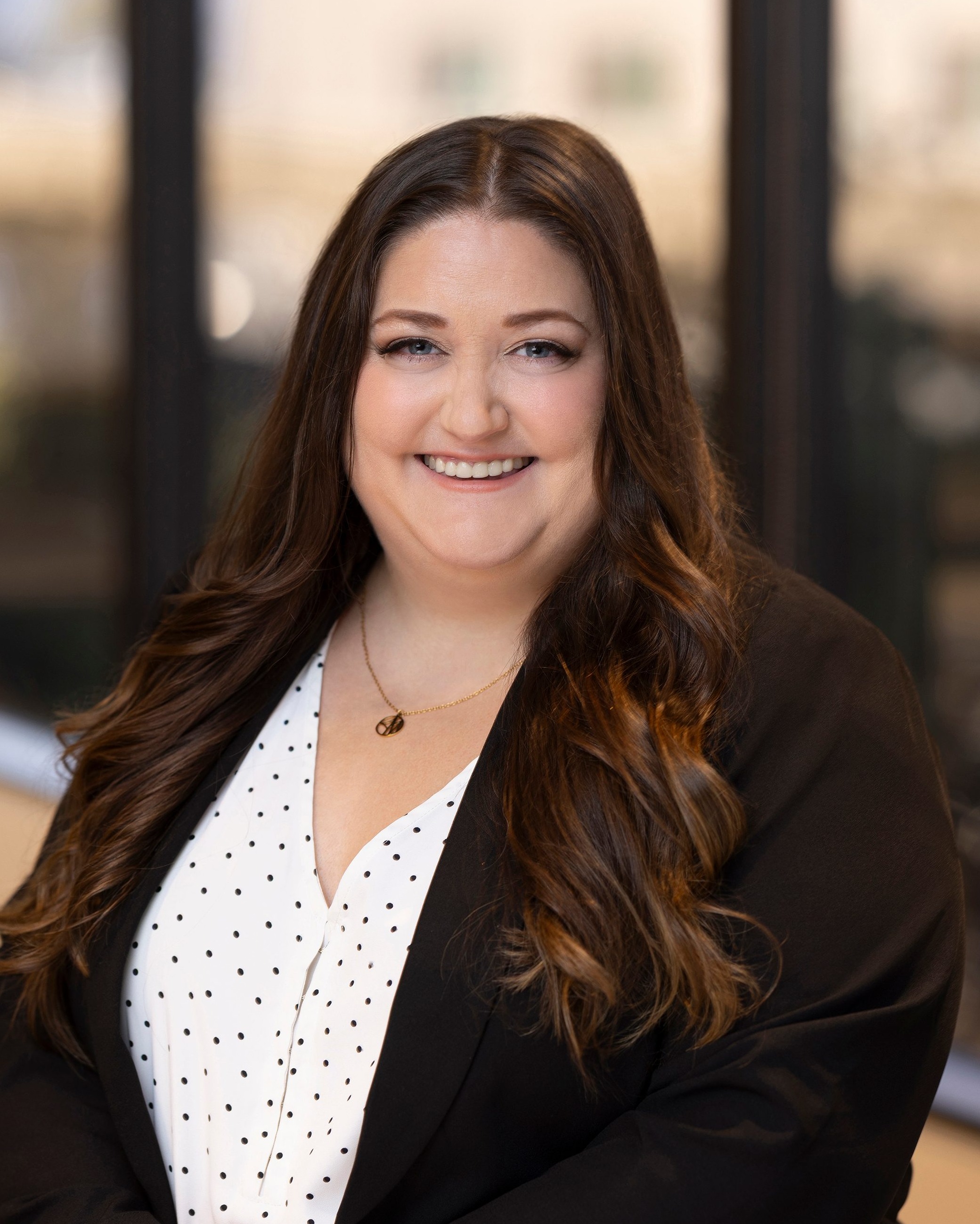 Katie Benedict, Chief Operating Officer of Post Acute Analytics, in a black blazer and polka-dot blouse in a modern office