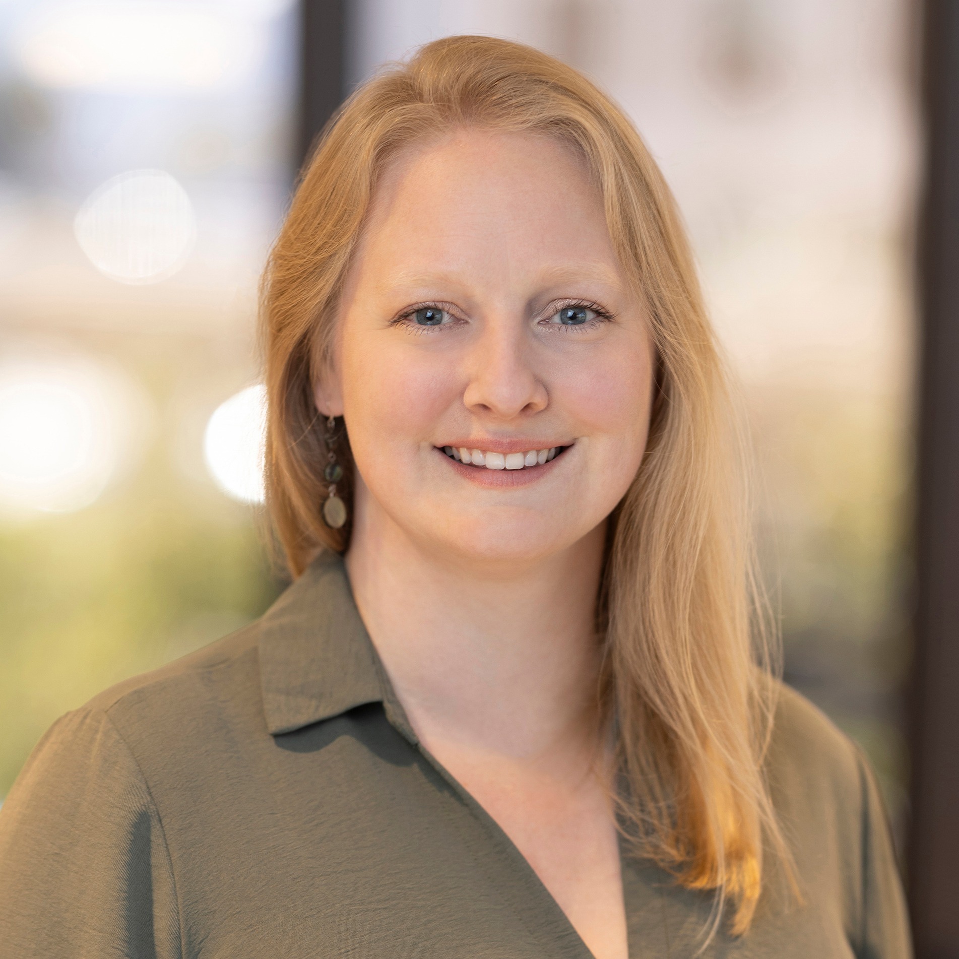 Seana Hall, Software Architect at Post Acute Analytics, in an olive green shirt in a modern office